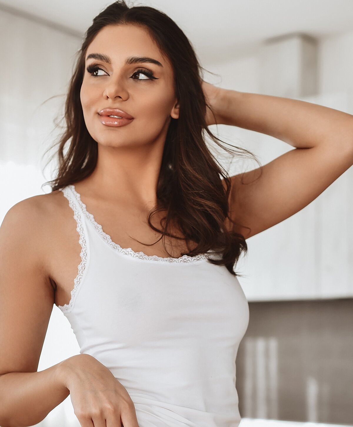 Woman in white tank top indoors, smiling.