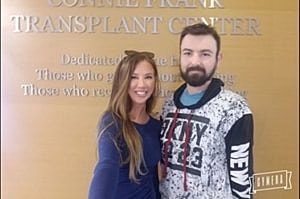 Two people smiling at a transplant center sign.