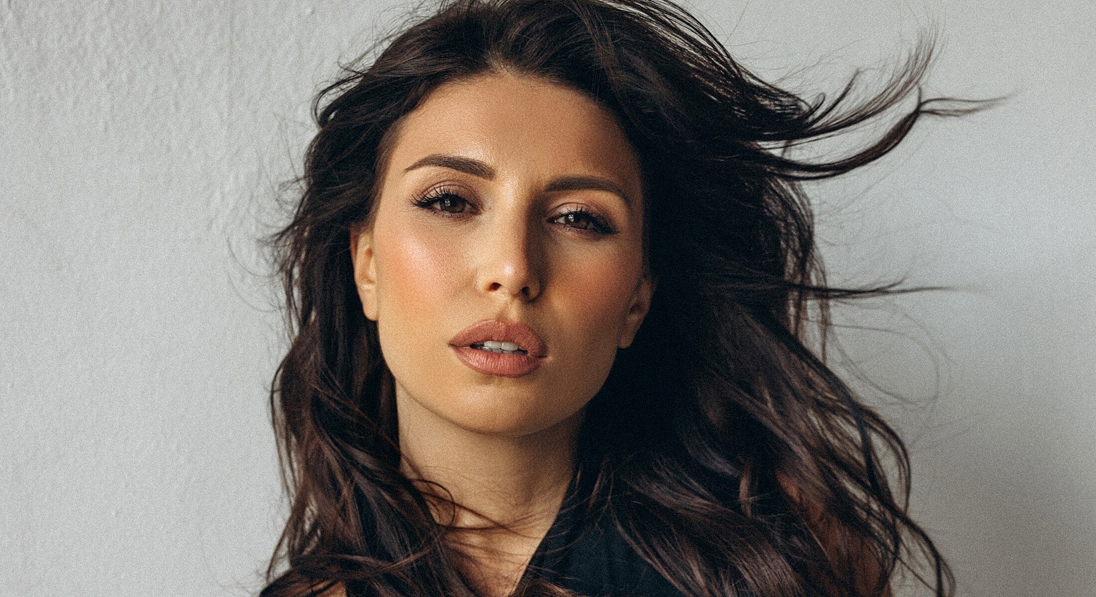 Woman with flowing hair, striking expression, neutral background.